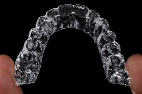 Invisalign dental aligner held between fingers against a black background for teeth straightening.
